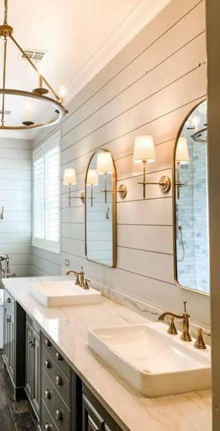 Brass faucets and arched mirrors above vessel sinks against a shiplap wall